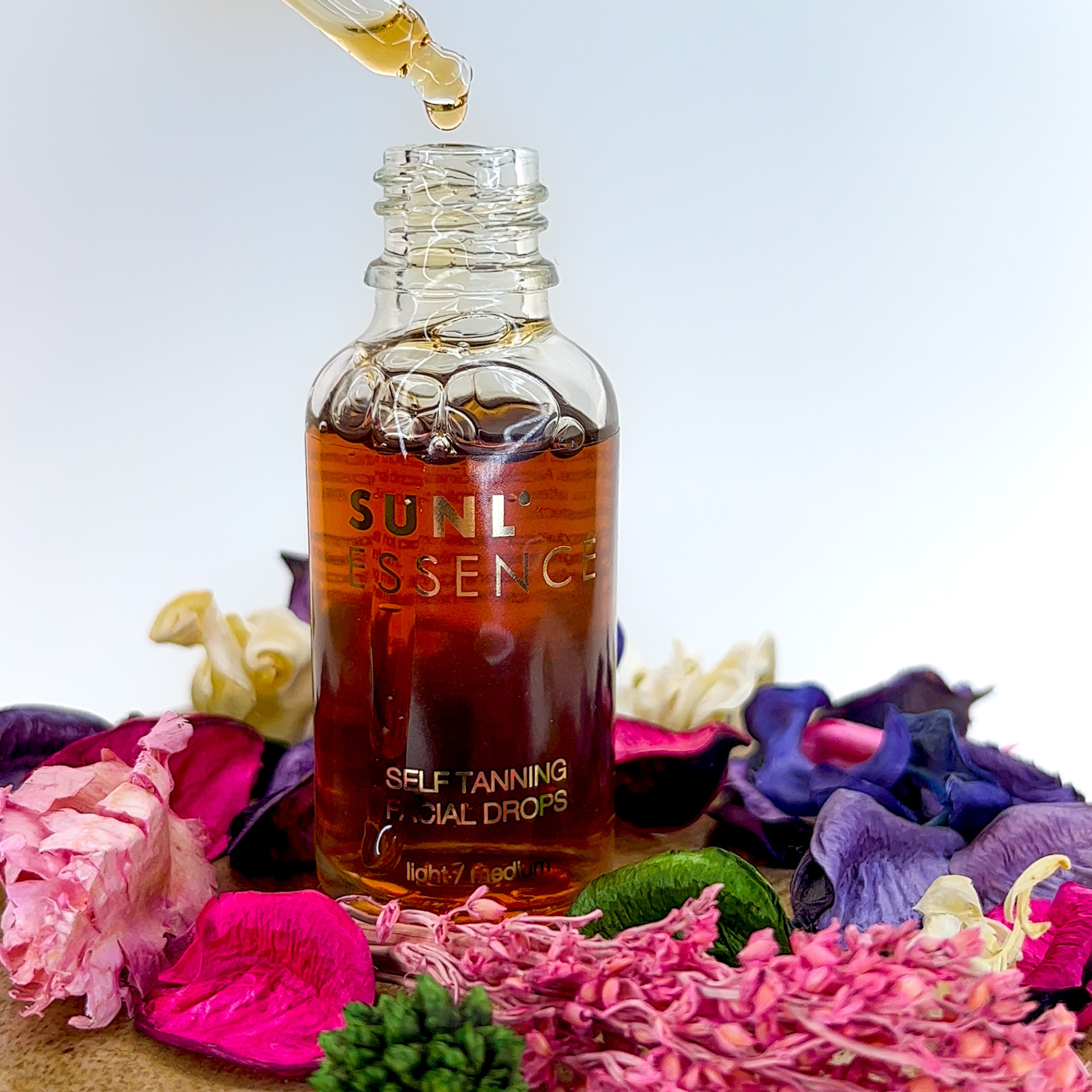 Kropelki samoopalające Onyx Sunl’essence w otoczeniu suszonych kwiatów. Naturalne składniki pielęgnują cerę i nadają jej ciepły, opalony odcień.