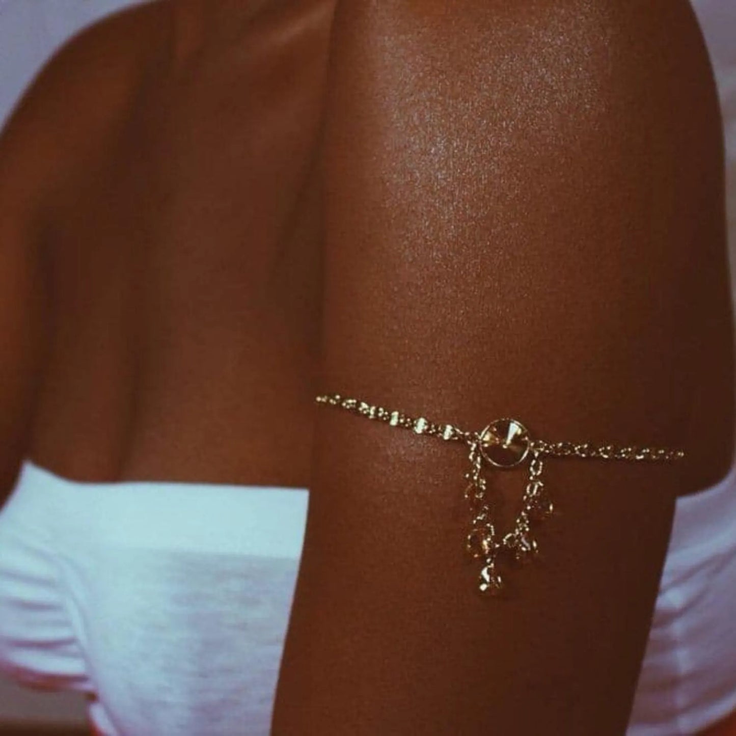 Zbliżenie na opaloną rękę kobiety ozdobioną złotą bransoletką, skóra ma wyraźny połysk i równy odcień po użyciu balsamu rozświetlającego Onyx La Playa