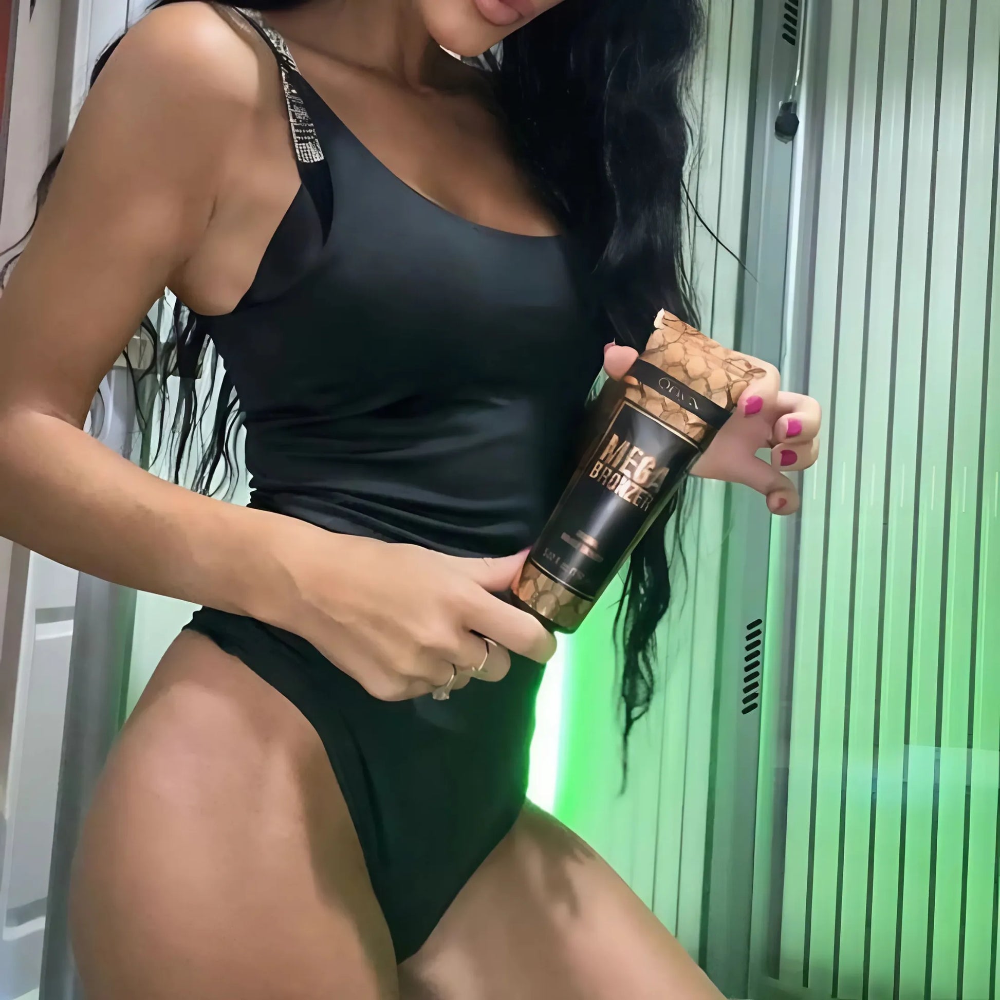 Kobieta w czarnym stroju kąpielowym trzyma balsam Onyx Mega Bronzer w kabinie solarium, pokazując kosmetyk do uzyskania głębokiej, złotej opalenizny