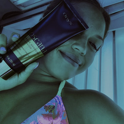 Kobieta trzyma balsam Onyx Toscana w solarium, uśmiecha się, światło lamp podkreśla niebieski odcień wnętrza i złoty połysk opakowania