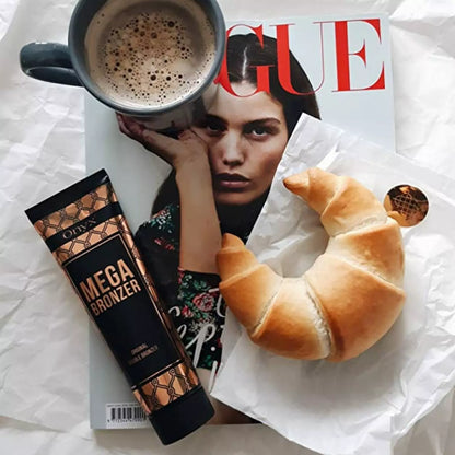 Tuba balsamu do opalania Onyx Mega Bronzer leży na magazynie Vogue obok filiżanki kawy i rogalika, tworząc elegancką kompozycję z produktem do brązującej pielęgnacji skóry